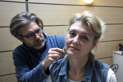 Dr. Emre Koçman examining an elderly woman before a facelift surgery in a modern wooden-paneled room.